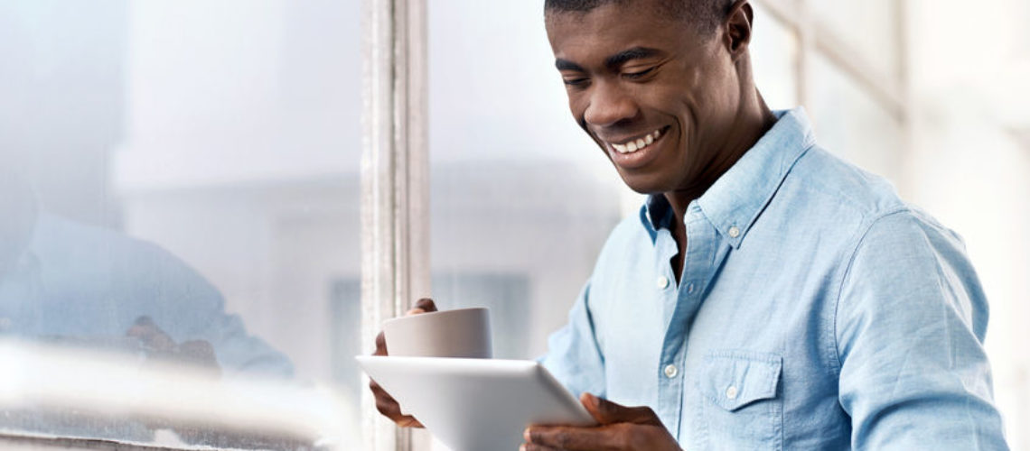40834406 - young successful black african man with morning coffee and tablet computer checking on news of investments