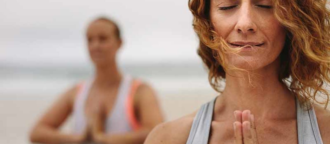 Close up of a woman with closed eyes practicing yoga at the beach. Women in fitness wear at the beach doing yoga with closed eyes and joined palms.